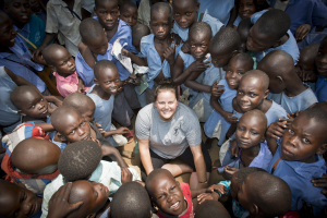 A white woman meets a group of friendly African children in Uganda. The children are happy and smiling.